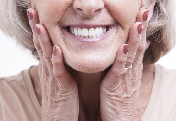An elderly woman holds her face while shining her beautiful, implant-support dentures.