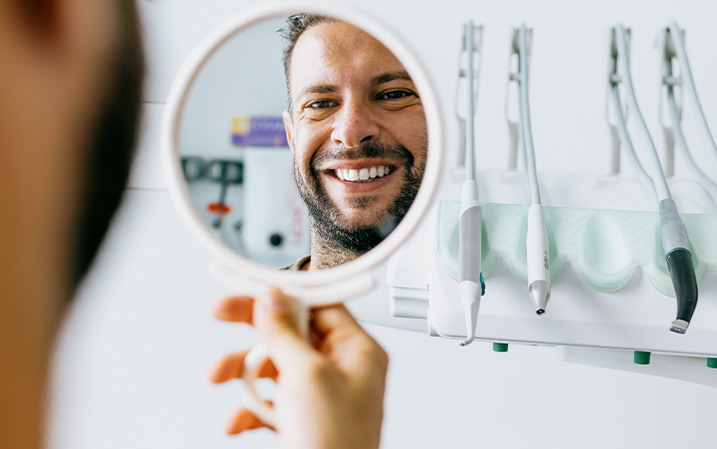 Man checking his freshly-cleaned teeth in a mirror