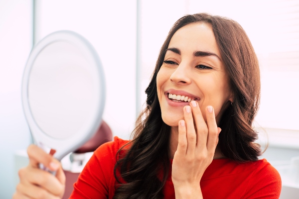 A smiling woman looks after teeth after recovering from dental implant surgery.