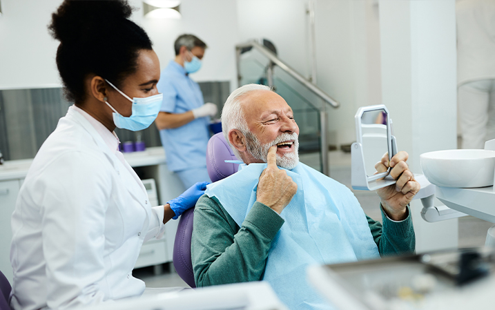 A dentist sitting with her patient as he checks his teeth